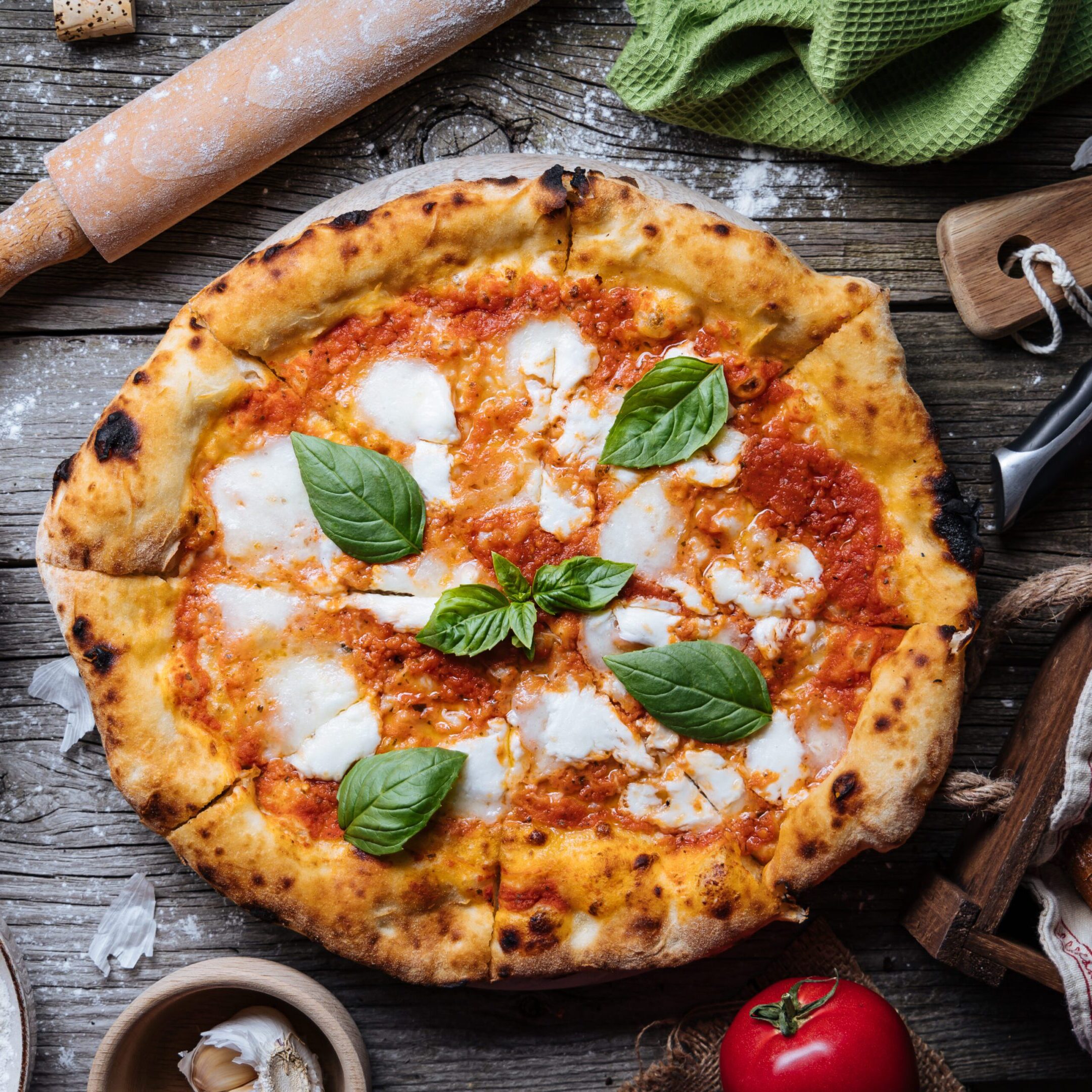 Italian Pizza Napoletana in Messy Kitchen with Cooking Ingredients Margherita pizza with fresh ingredients on table.
